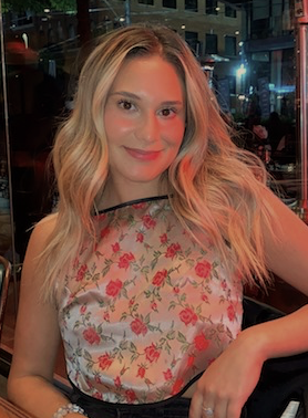 Picture of Alexantria, smiling at the camera outdoors. Wearing a rose pink top with red roses.