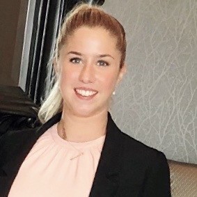 Picture of Anna, smiling at the cameraa wearing a pink blouse and a black blazer