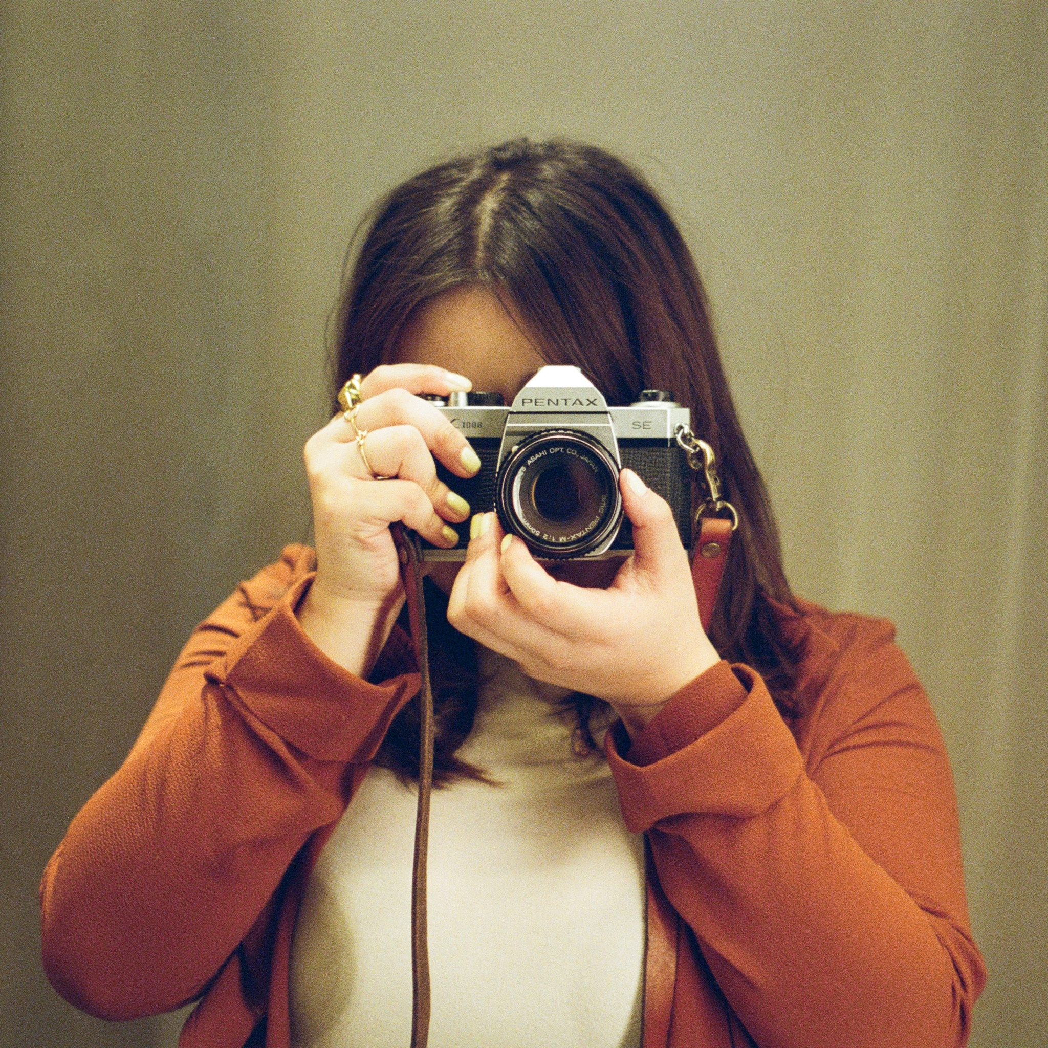 Portrait of Chalista taking a picture with her camera, wearing a red jacket and while blouse