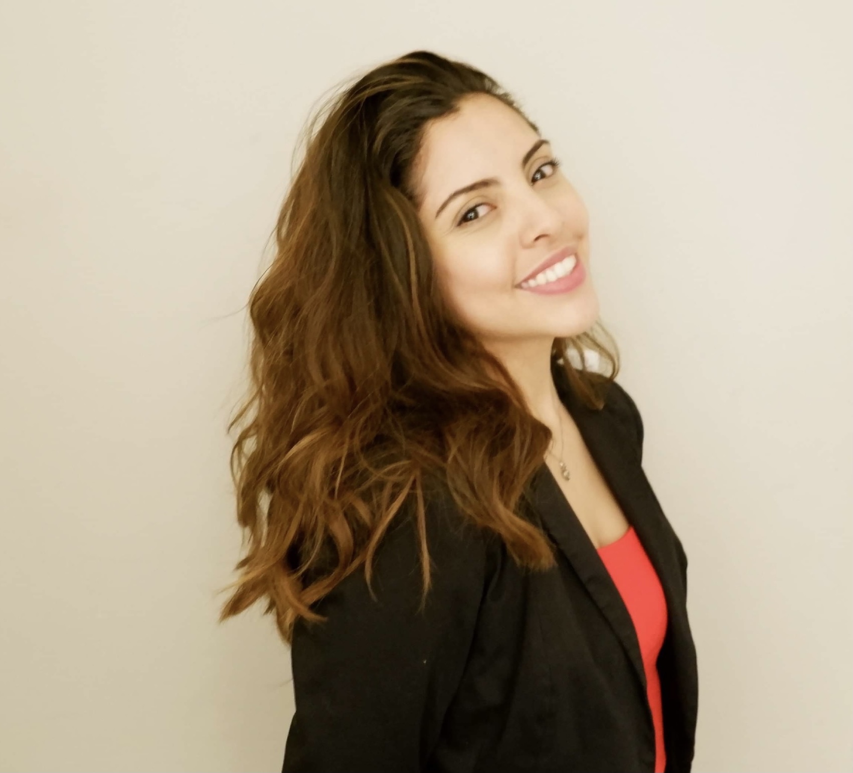 Portrait of Maria, smiling and posing with a black blazer and a red tank top