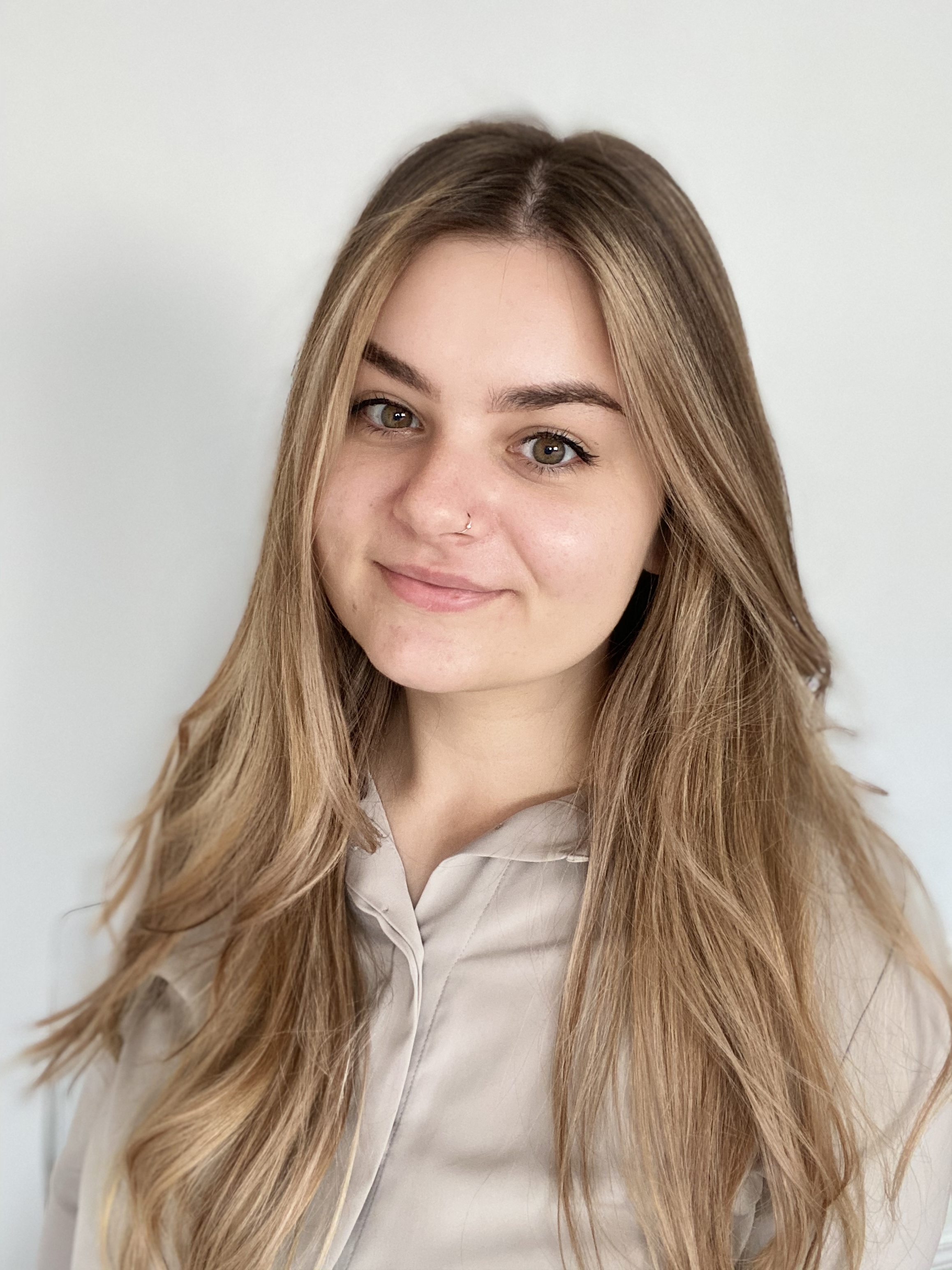 Portrait picture of Victoria, smiling and wearing a beige shirt.