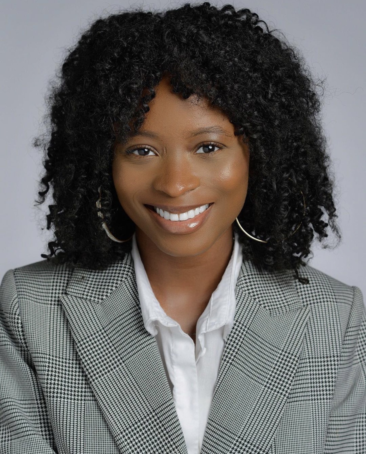 Portrait of Zane, wearing a grey/black/white blazer and a white blouse