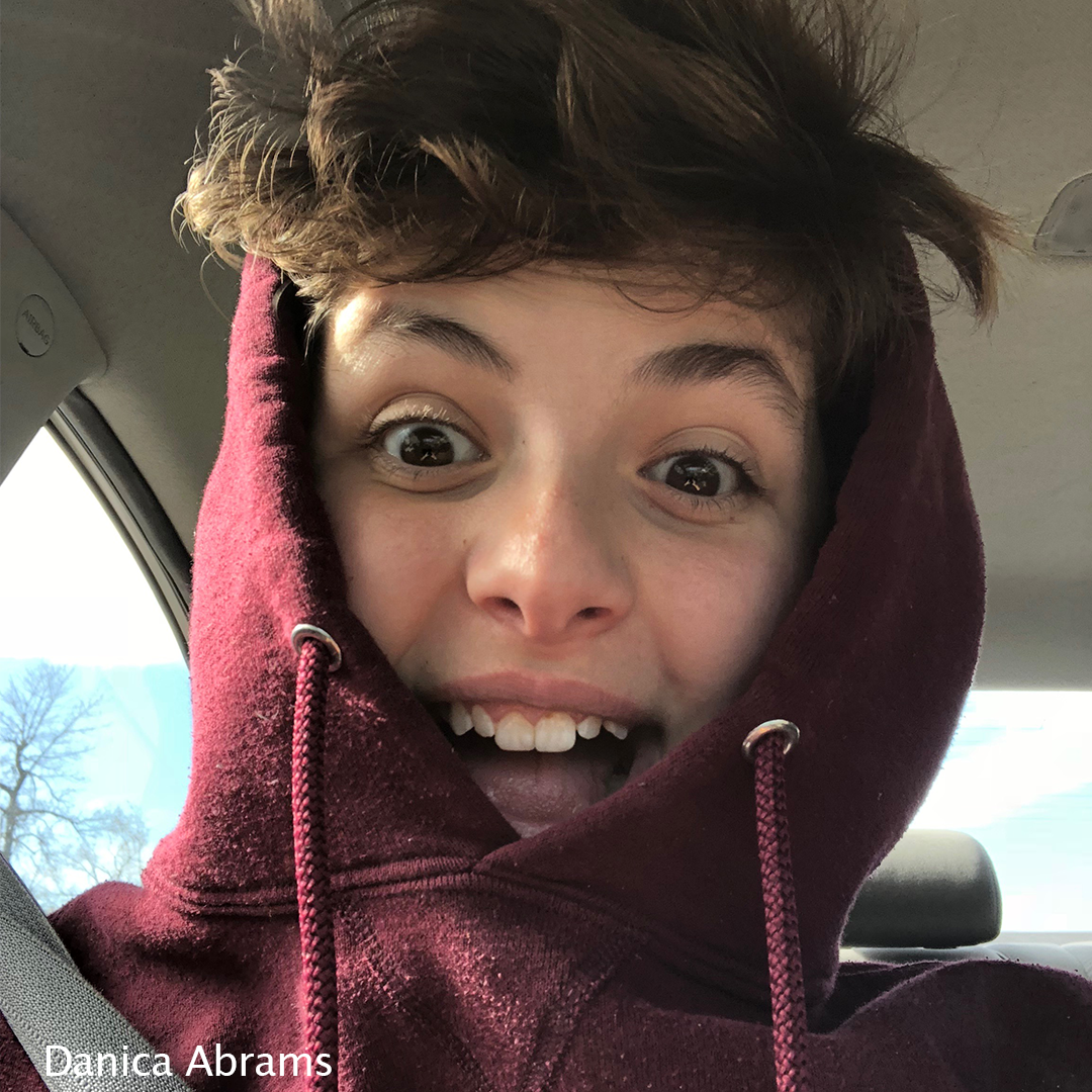 Photo of Danica wearing a hooded sweatshirt with a surprised and happy expression