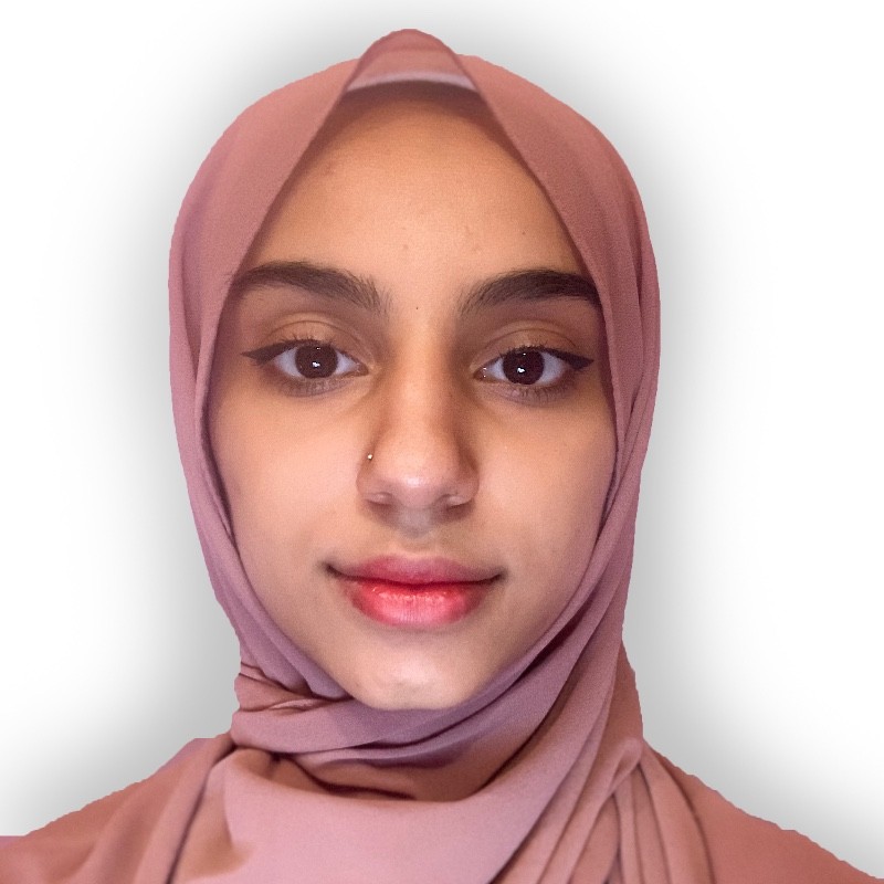 Picture of Maymona posing to the camera against a white wall wearing a salmon pink hijab