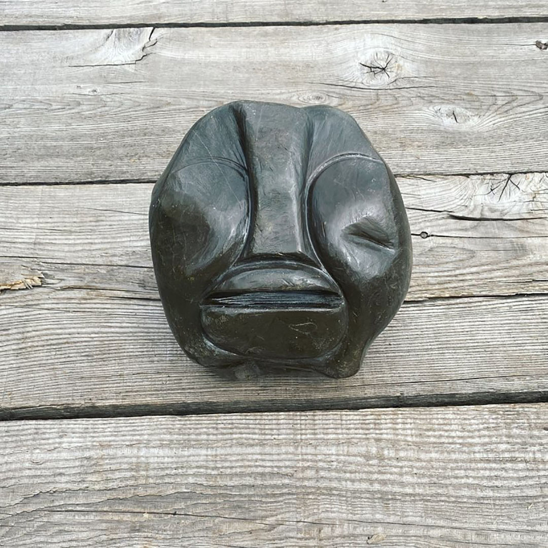 A natural hand carved stone resembling a human face, with an exaggerated nose and lips. The stone has been sanded to be smooth to the touch and burnished with olive oil to bring the true color out from the stone. (Black)