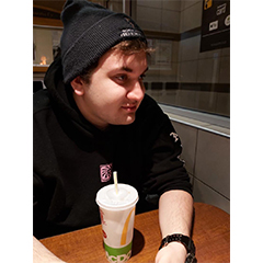 Picture of Aleksandar sitting and wearing a black hoodie and having a coffee