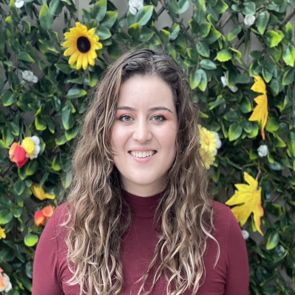 Picture of Vanessa, outdoors with flowers behind her, wearing a red turtle neck shirt