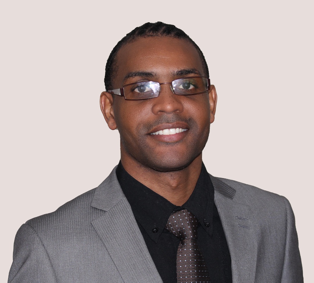 A picture of Edgar smiling at the camera, dress with a suit and tie, and wearing eye glasses.