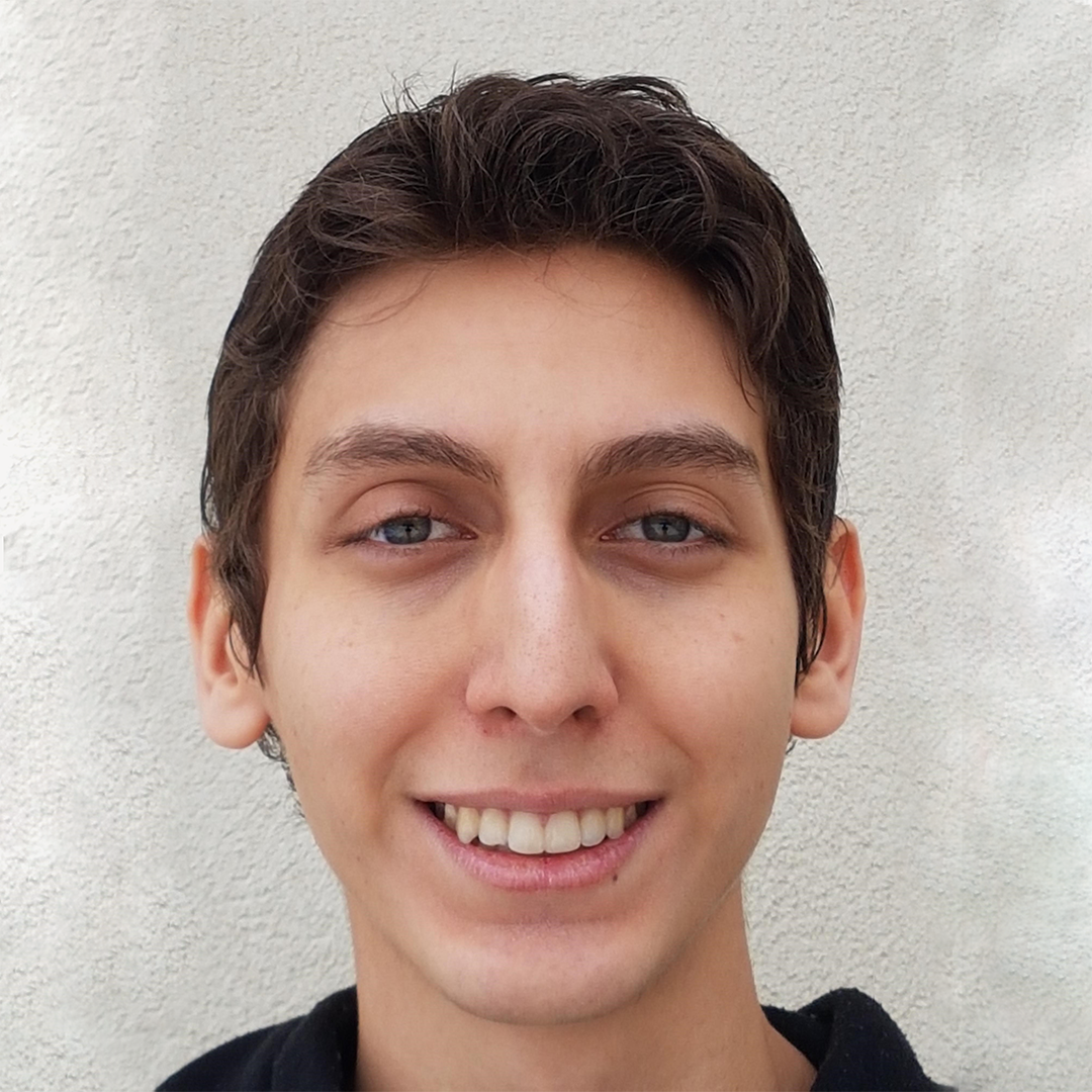 Justin, light-skinned person with short brown hair, smiling in front of a rough wall texture on a cloudy day
