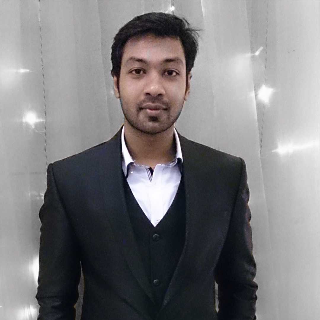 A picture of Nahid wearing suits and standing in front of lighter color wall.