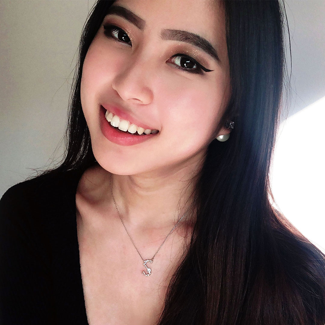 Sammie, a Korean young woman with long dark brown hair with makeup, indoors in a bright day. she is wearing black v neck top, smiles at the camera.