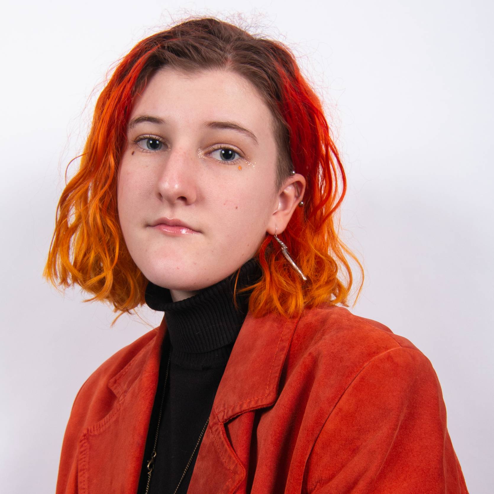 Photo of FMTV Graduate Leah Godwin, they have fire coloured hair and are wearing a bright orange jacket