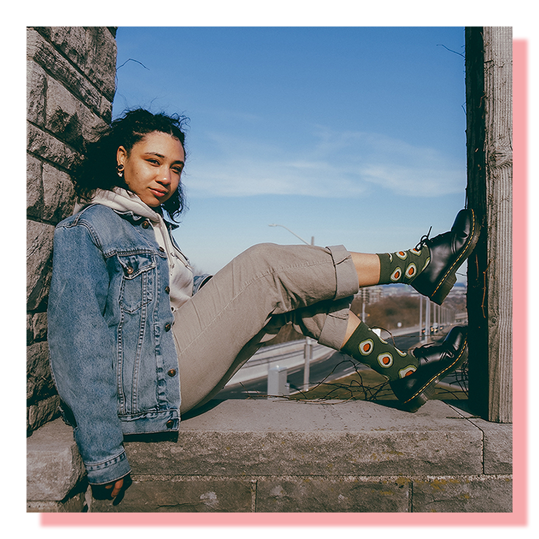 A model wearing avocado socks sitting with in a small enclosure with her feet propped up on the wall
