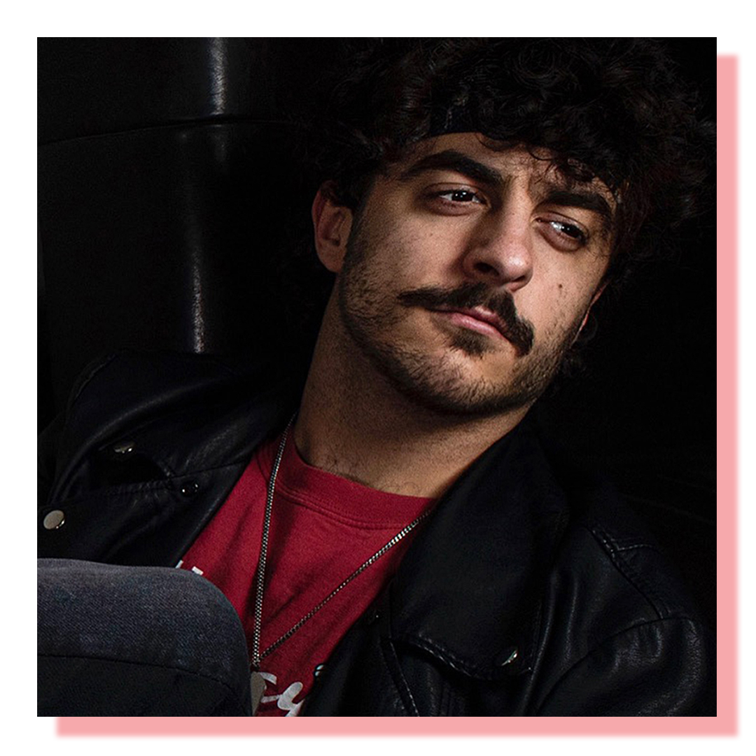 Head and shoulders self-portrait of a man with a mustache, black leather jacket and red top.