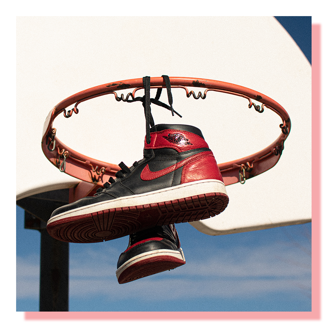 Sneakers, black and red, tied together and hung up on the rim of a basketball net.