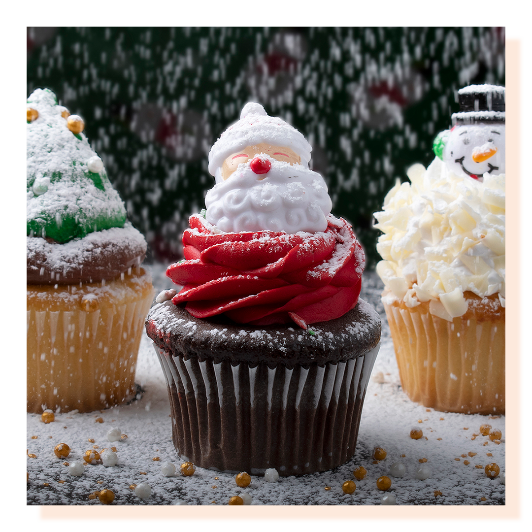 Three cupcakes with santa and Christmas holiday decorations. Sugar snow is falling on cupcakes.