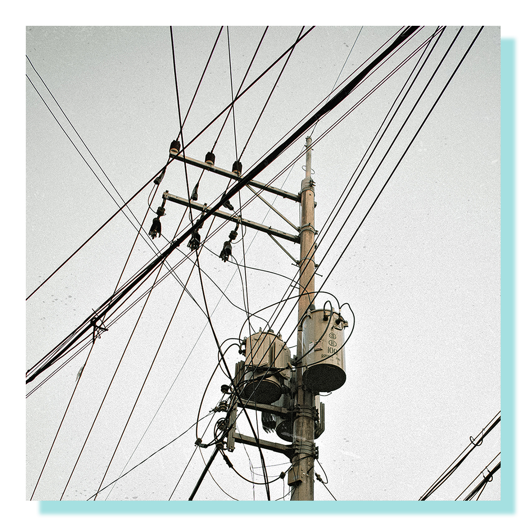 Black and white photo of tangled telephone poles and wires.