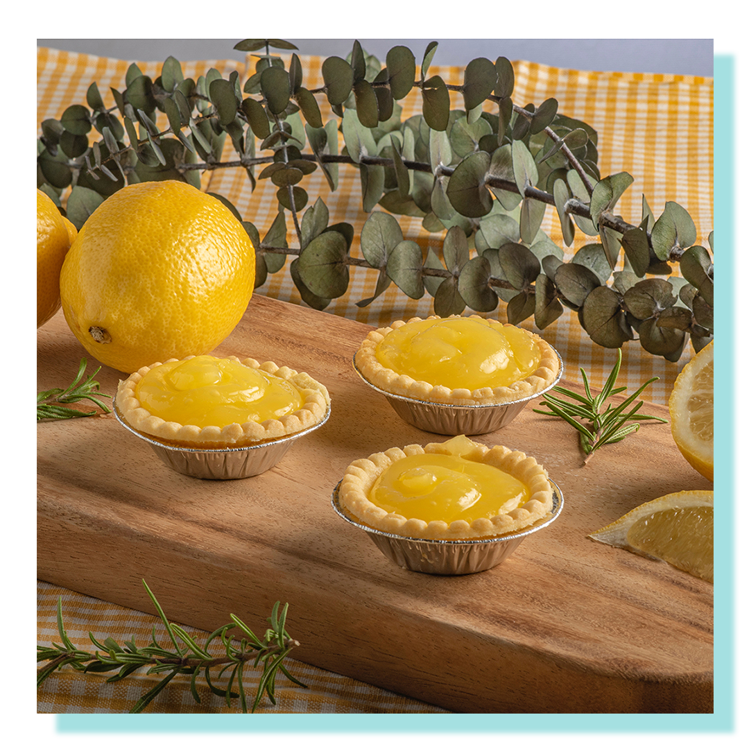 Lemon Tarts displayed on a wooden board and gingham tablecloth and decorated with lemon wedges and eucalyptus.