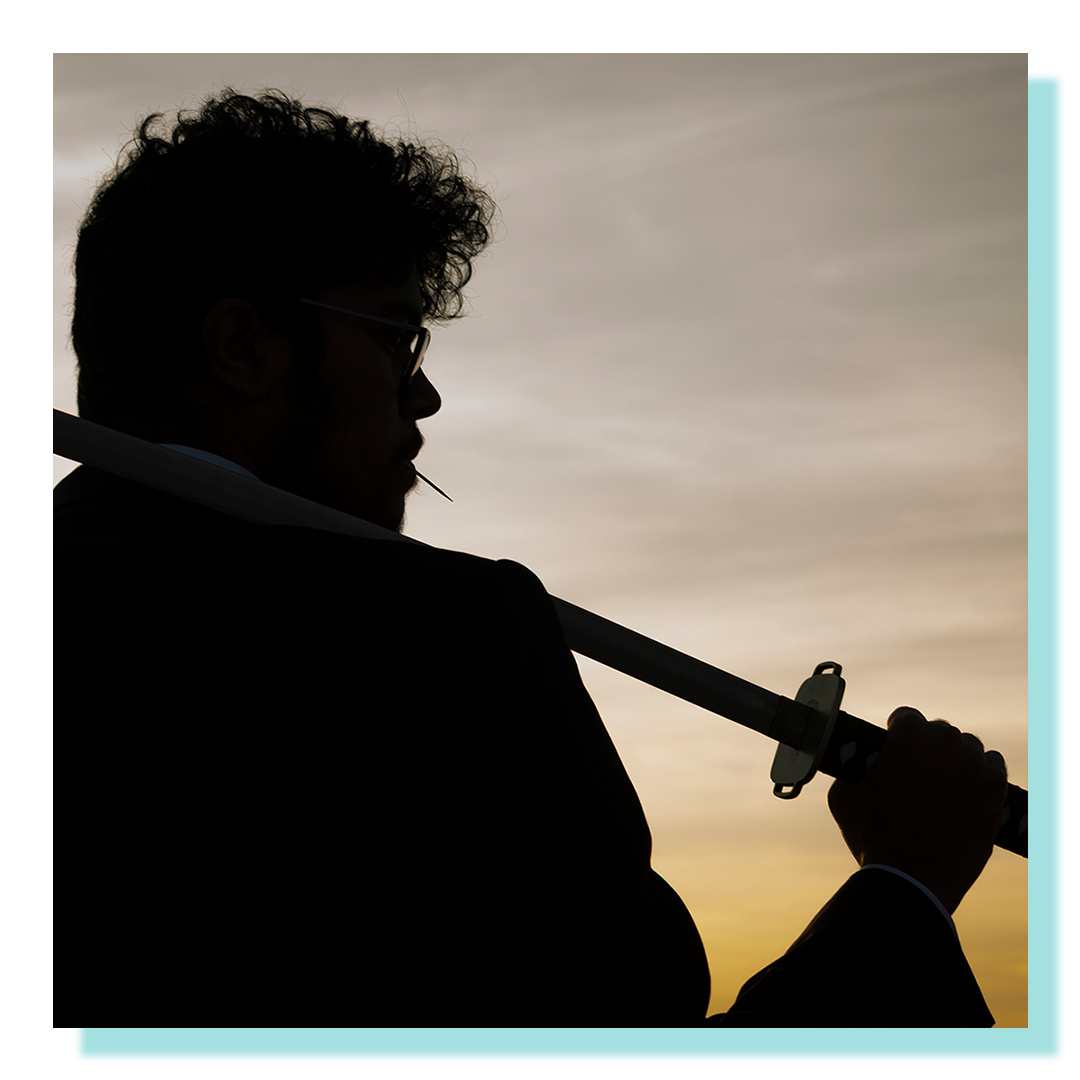 A mysterious man holding a katana over his shoulder at sunset