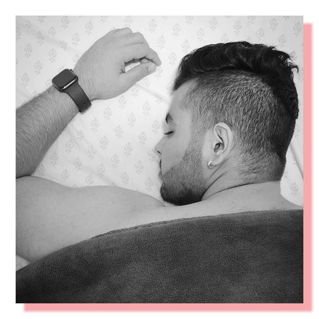 Black & white portrait of a man sleeping face down in bed under the covers.