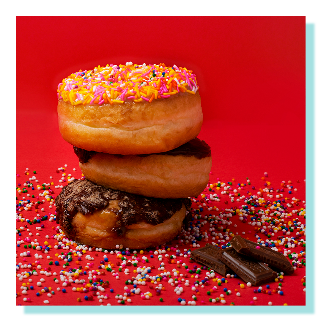 Three donuts stacked on top of each other on a red background with chocolate chunks and sprinkles.