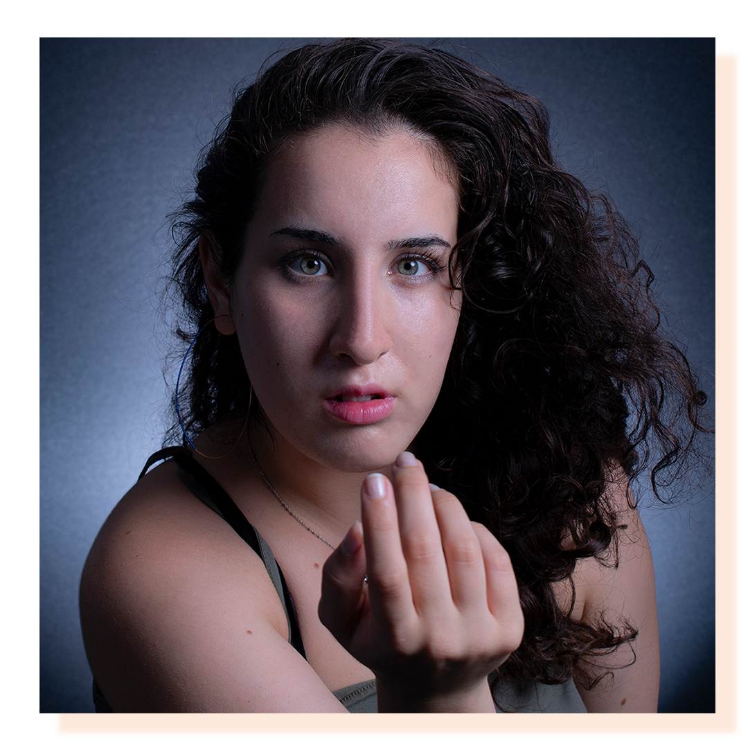 A close up headshot of a woman looking into the camera with hand near the face.