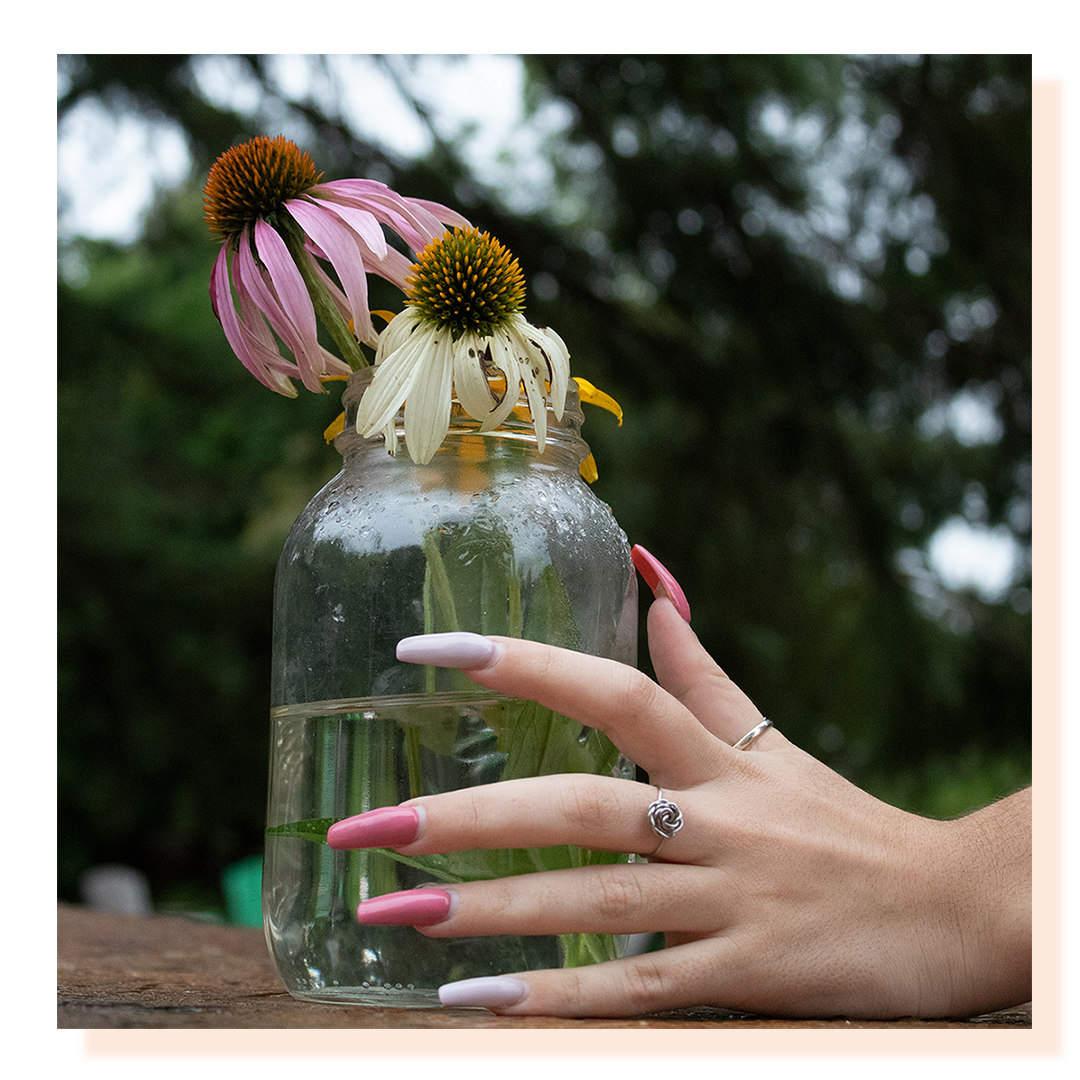 A mason jar holding water and flowers, with a woman’s hand wrapped around it.