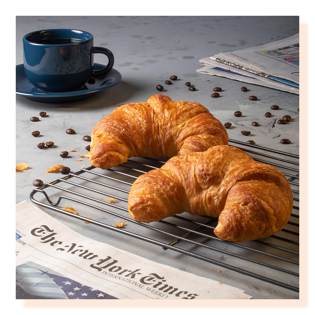 Croissants cooling on a rack with the New York Times and a cup of coffee, coffee beans scattered around.