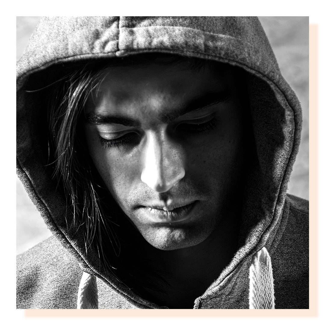 A close up portrait in black & white of a man wearing a hoodie looking down.