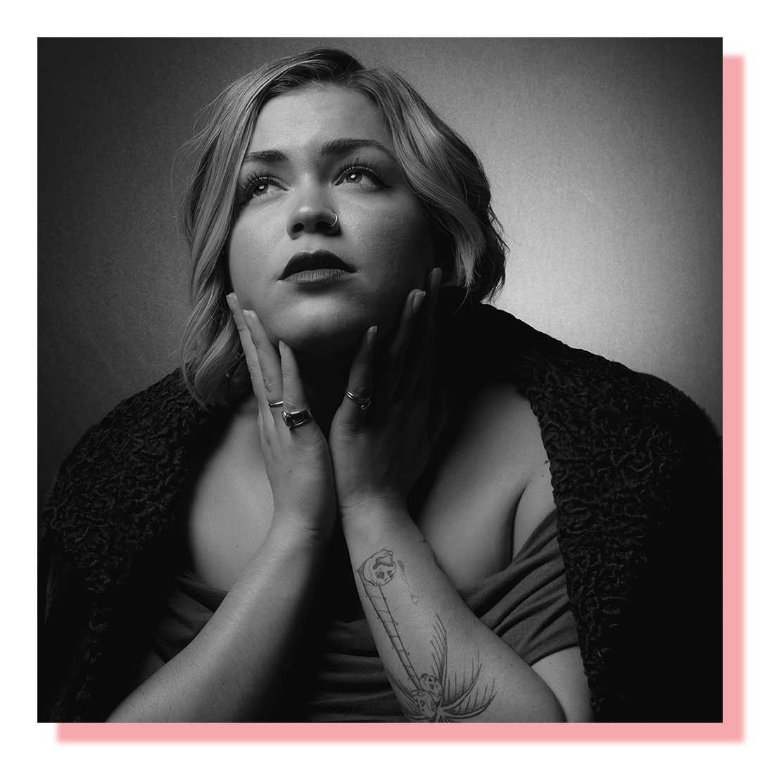 Woman dressed in black holding her neck with two hands. Dramatic studio lighting.