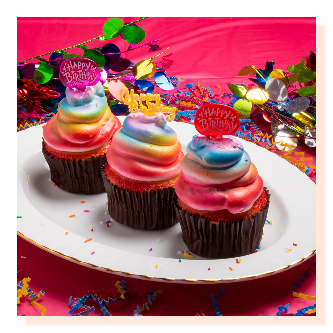 Three multi-coloured cupcakes on a white plate
