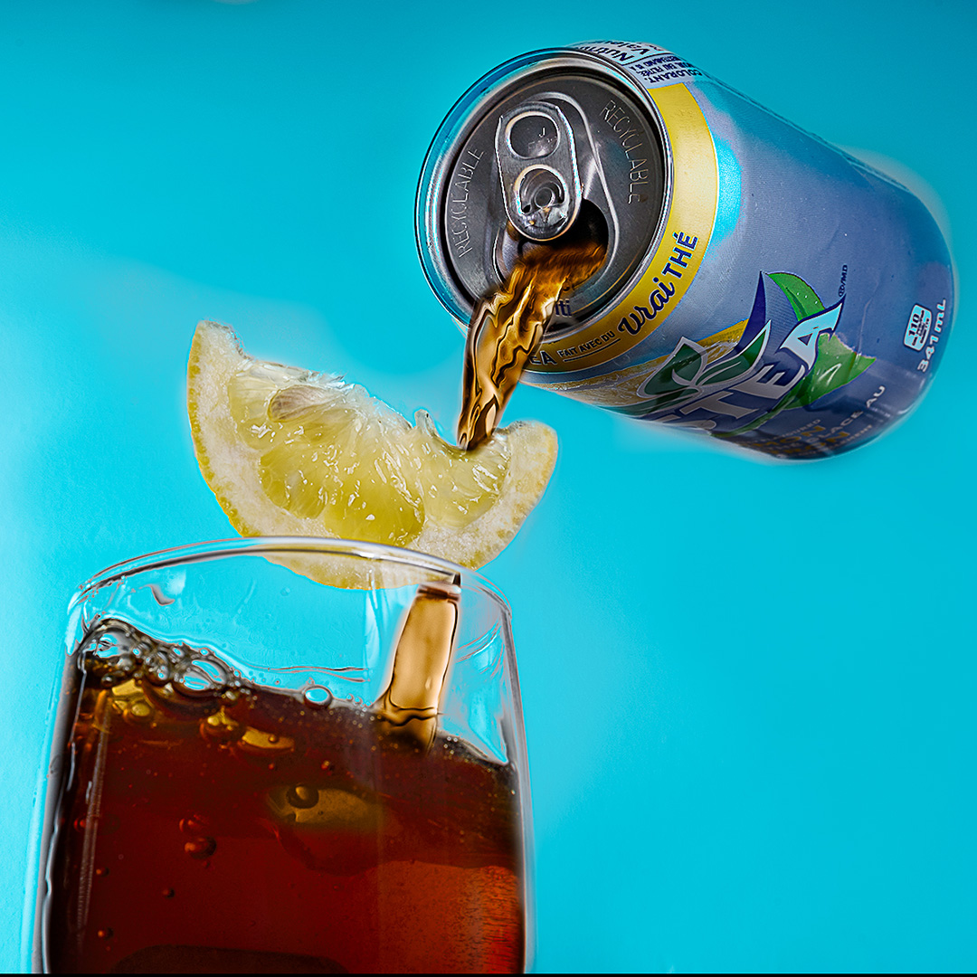 image is a can of Nestea pouring liquid into a glass with a slice of lemon falling into the glass as well.