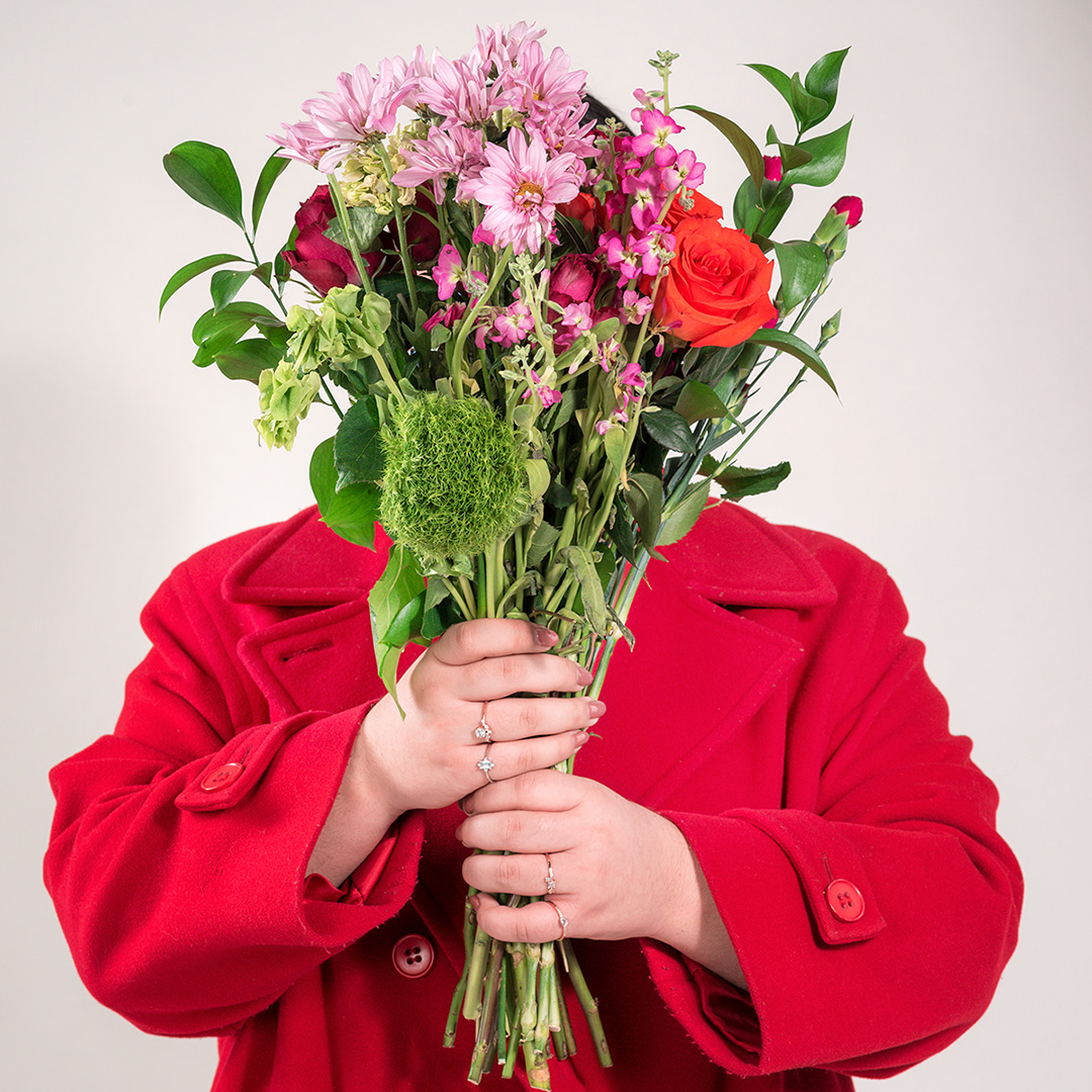 Women wearing a red jacket, holding a Bouquet of flowers in front of her face