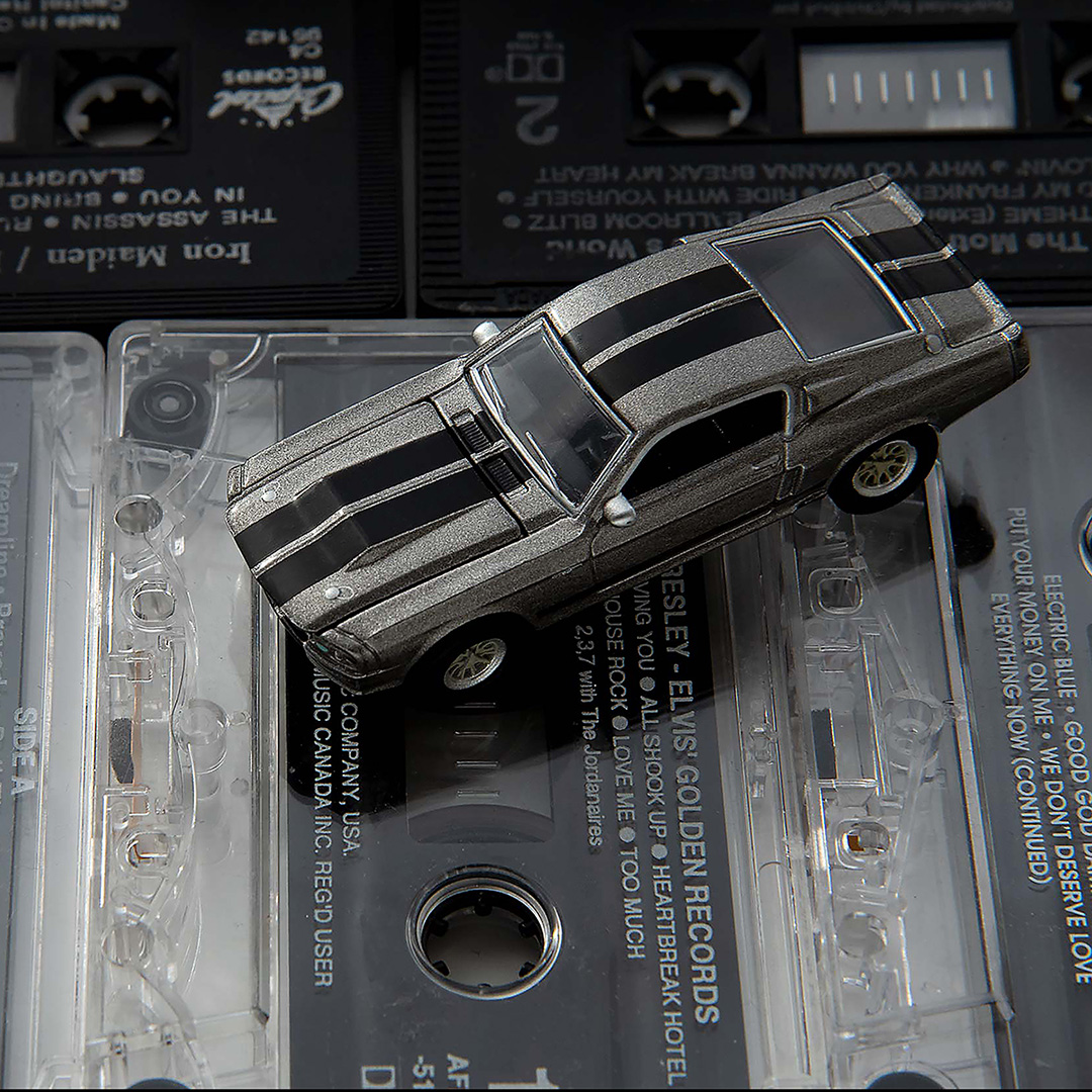 Silver Ford Mustang toy car viewed from above sitting on top of old cassette tapes