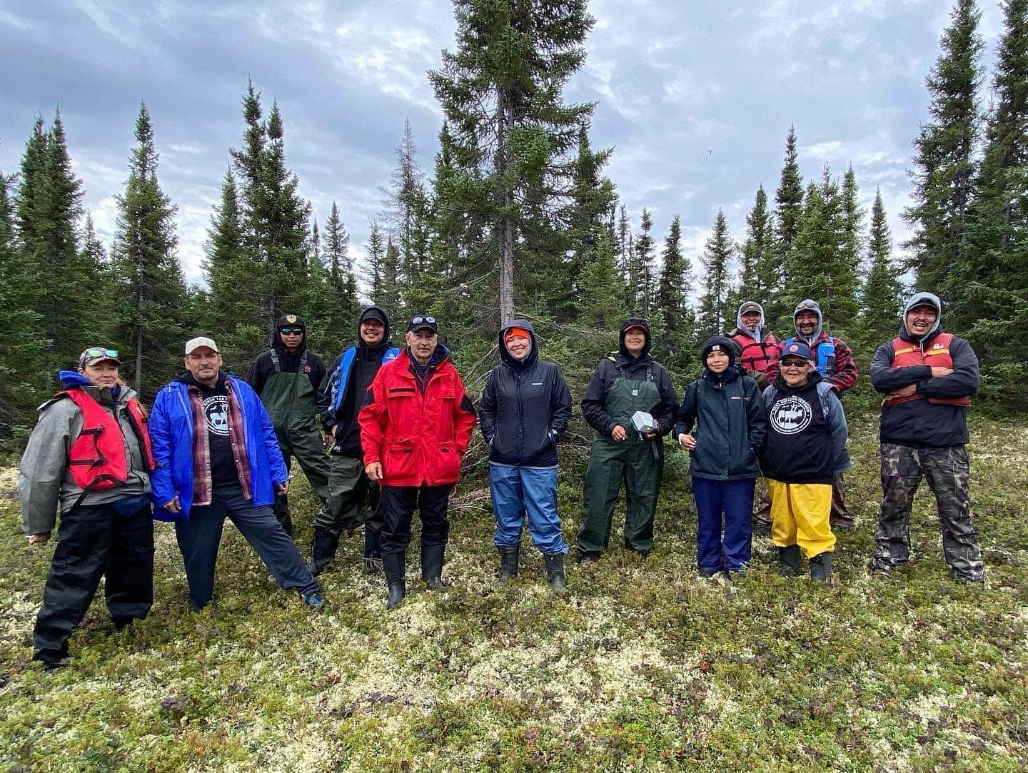 A group of land guardians from the Seal River Watershed Alliance stand surrounded by trees and moss during a canoe trip