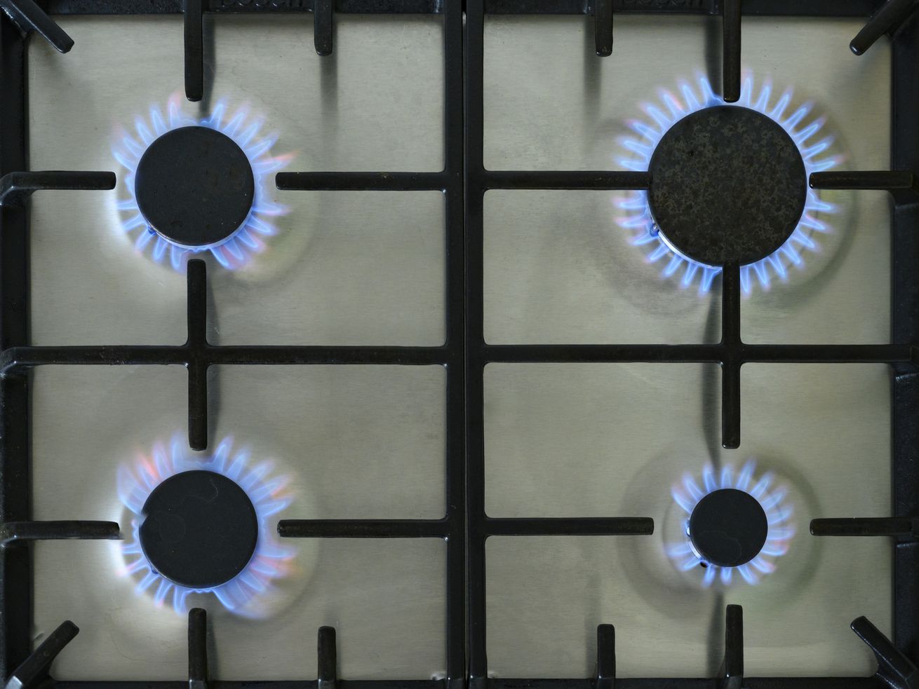 Four lit gas burners on a stove, seen from above.