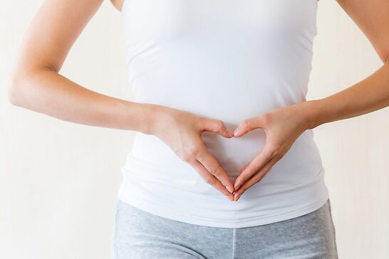 A woman forming a heart with her hands over her stomach area.