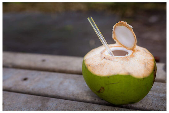 A green coconut with a straw hanging outside of an opening.