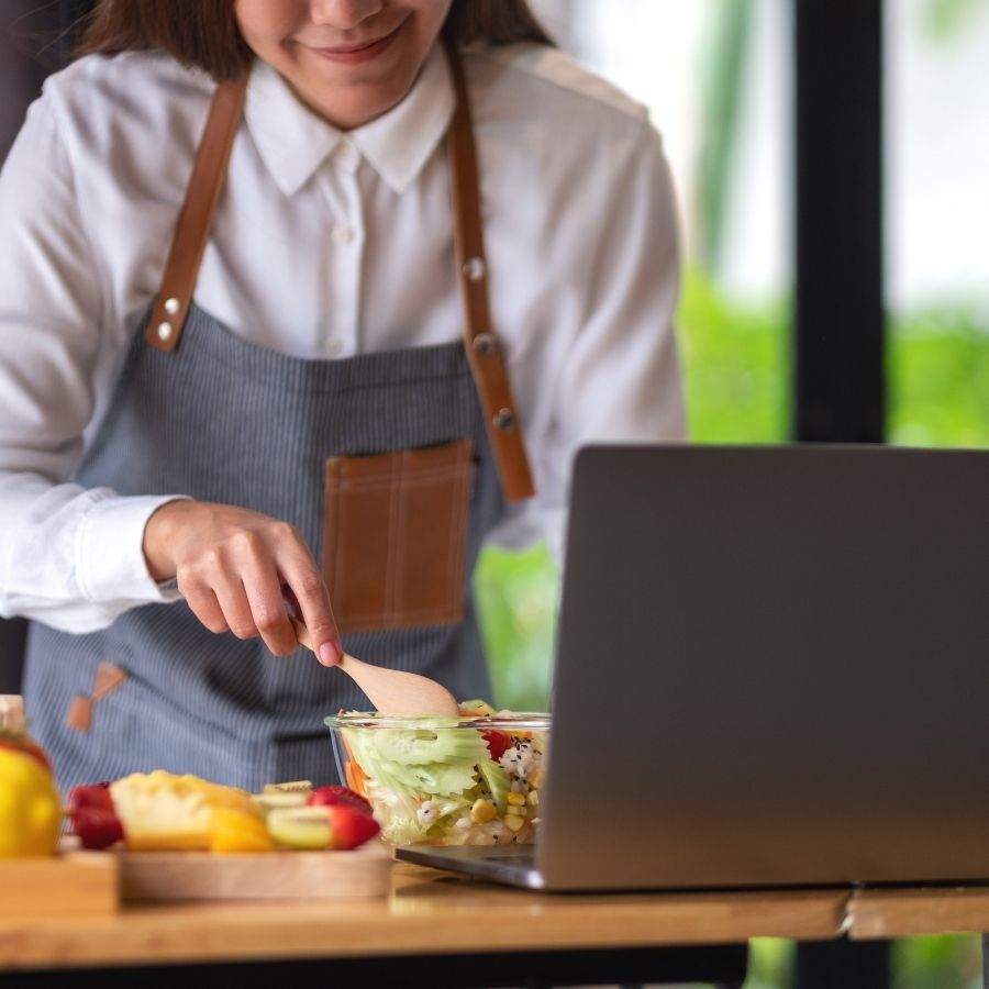 A woman cooking while watching computer screen.