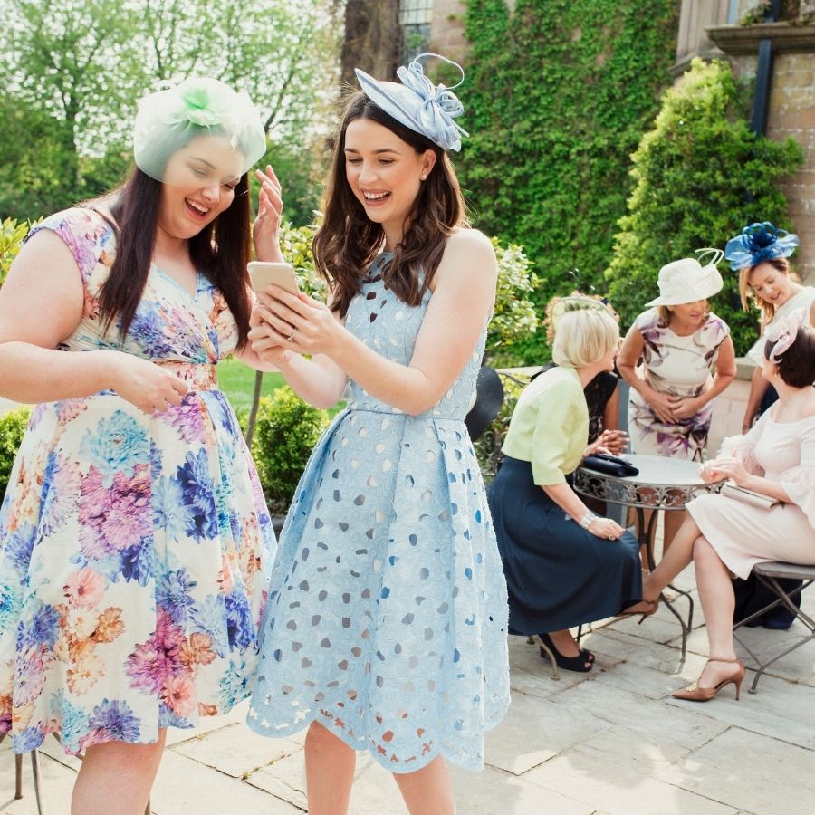 2 female wedding guest recording video message on phone.