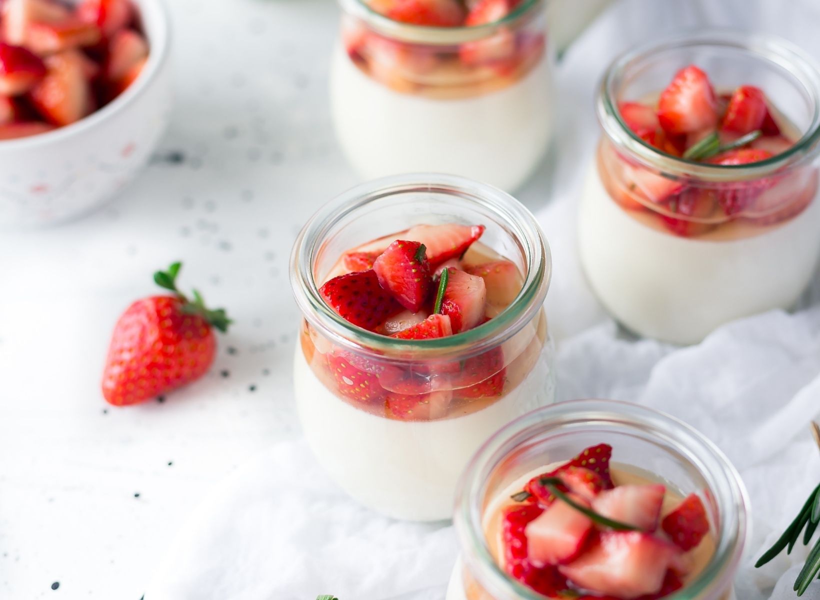 Jars of plain yogurt, a low-glycemic snack, with sliced strawberries on top