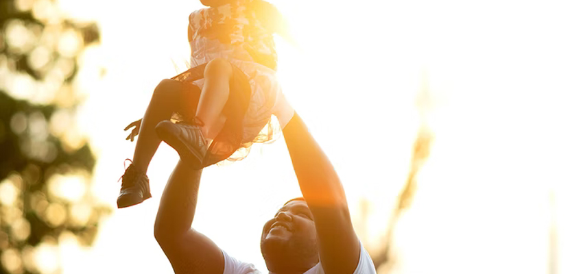 A dad holding his daughter in the air on a sunny day
