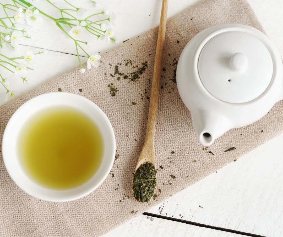 brewed green tea in a cup alongside a teapot