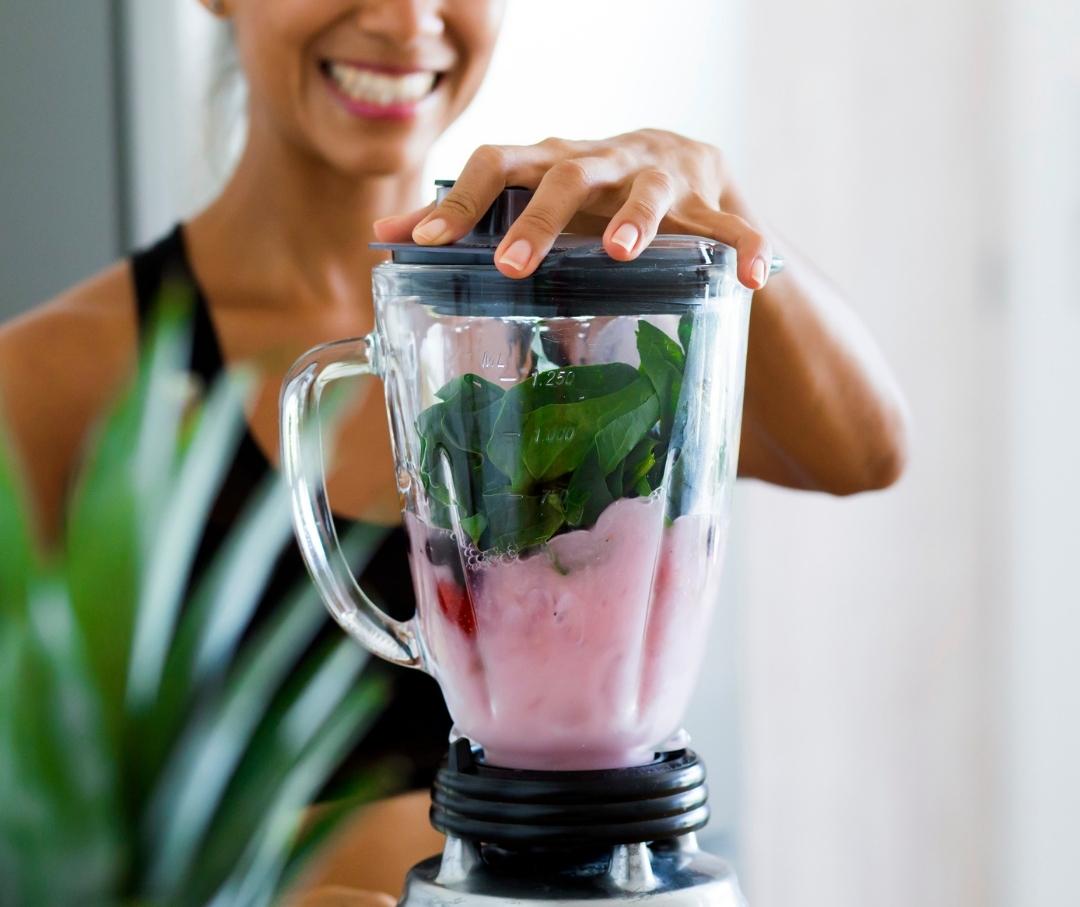 woman blending a smoothie with whey protein, berries, and greens