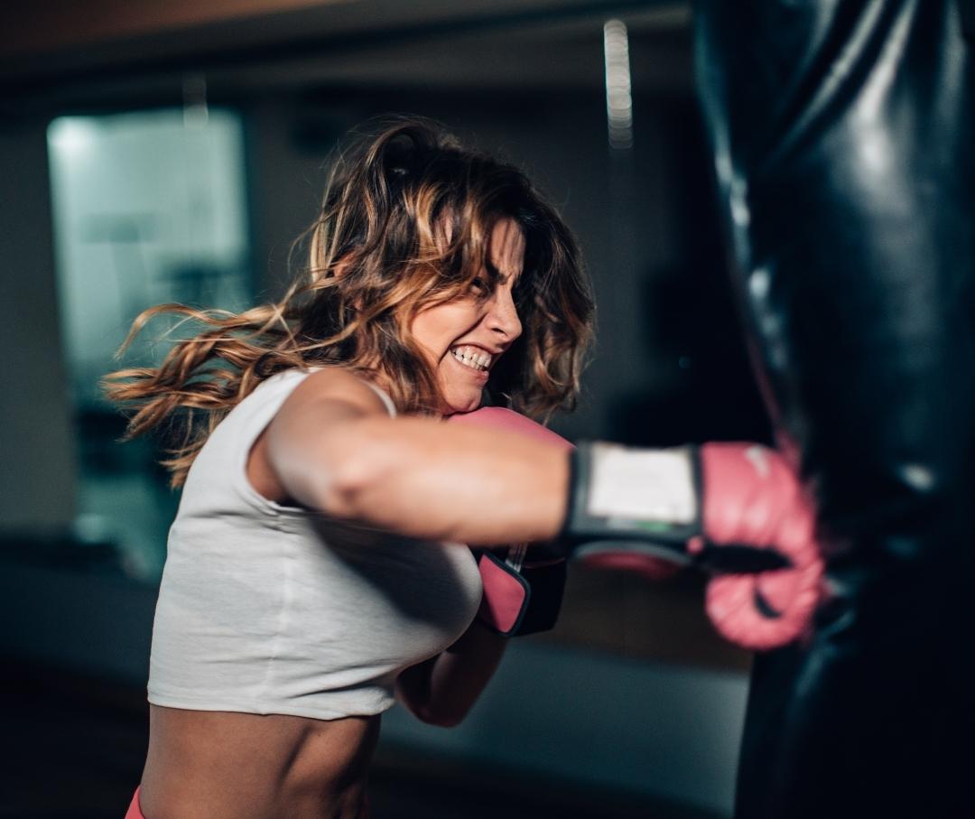woman in boxing gloves looking angry and hitting a punching bag