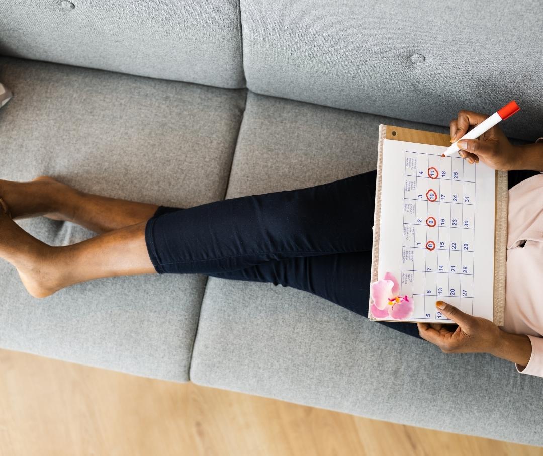 woman sitting on a sofa with a calendar on her lap, marking off dates