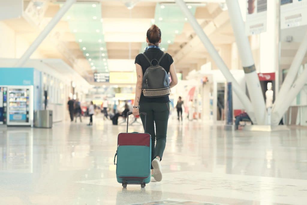 Back view of woman pulling her luggage strolling inside the airport terminal