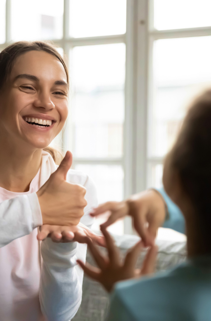 A support worker smiles while teaching sign language to a young kid