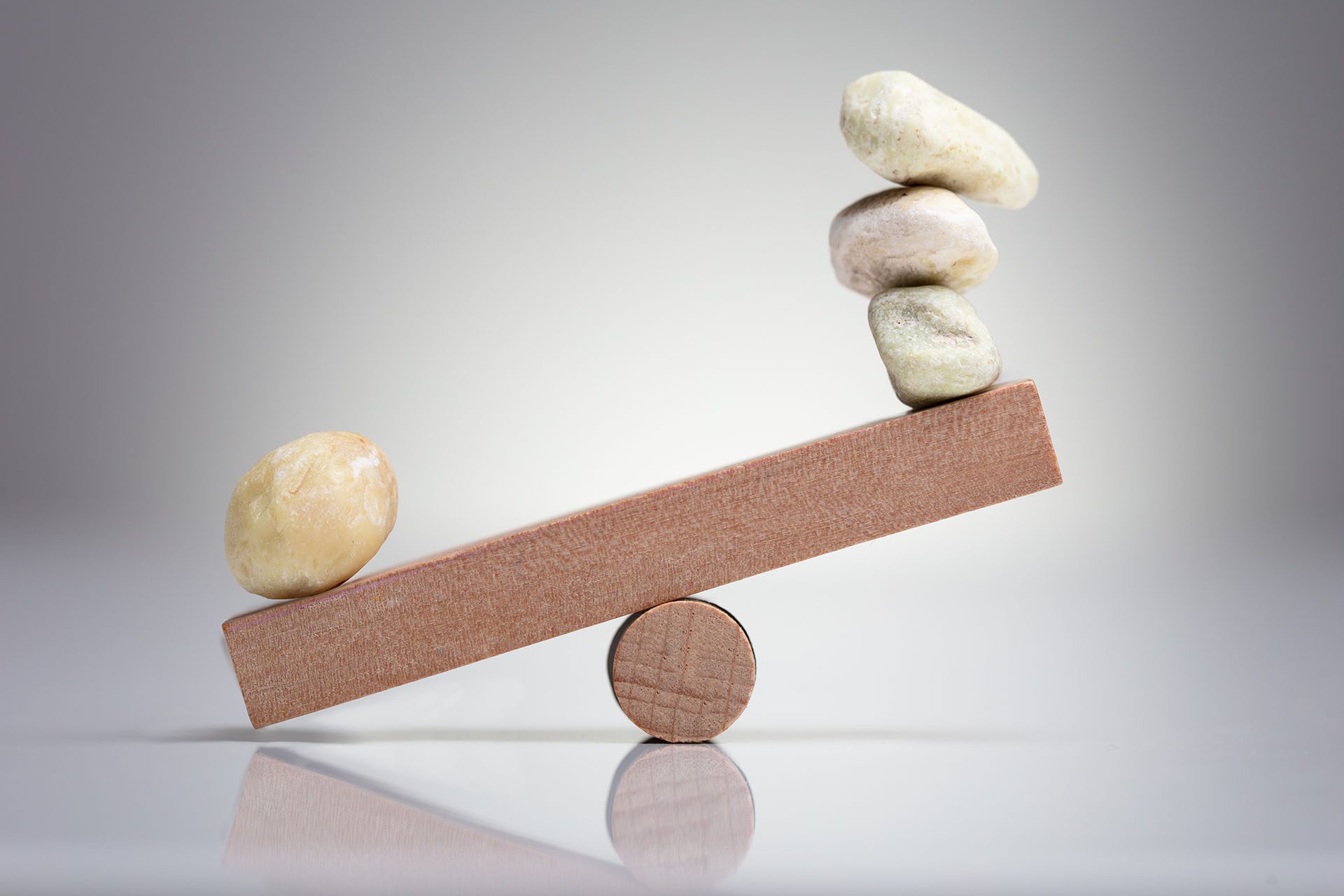 Pebble Stones Balancing On Wooden Seesaw Over The White Background