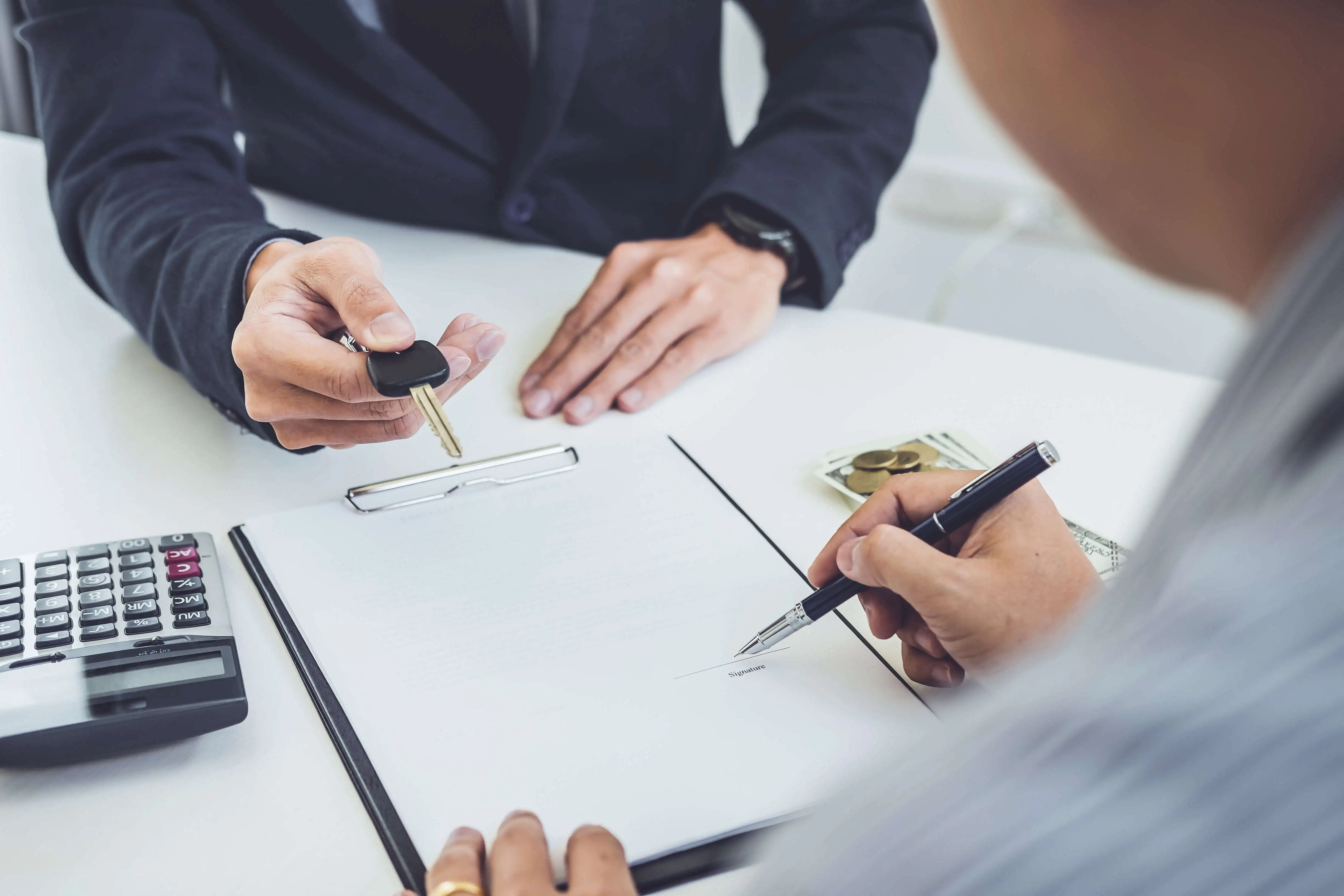 A person signing a car contract with a person across from them handing over car keys